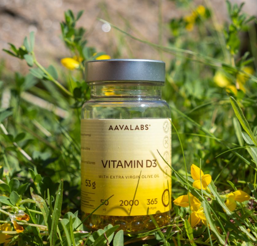 Flasche Aavalabs Vitamin D3 inmitten von grünem Gras und gelben Blumen.
