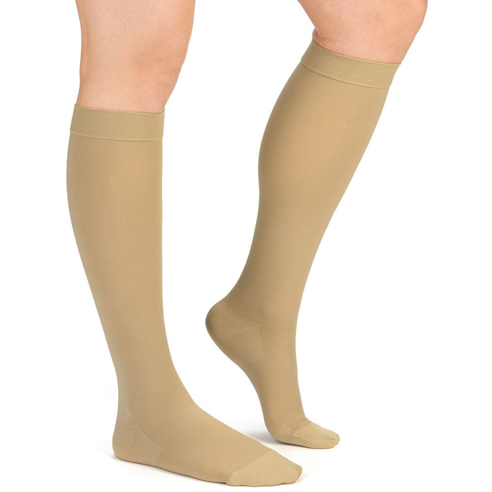 Beine mit hautfarbenen Kompressionsstrümpfen. Die Strümpfe reichen bis zum Knie. Der Hintergrund ist weiß.