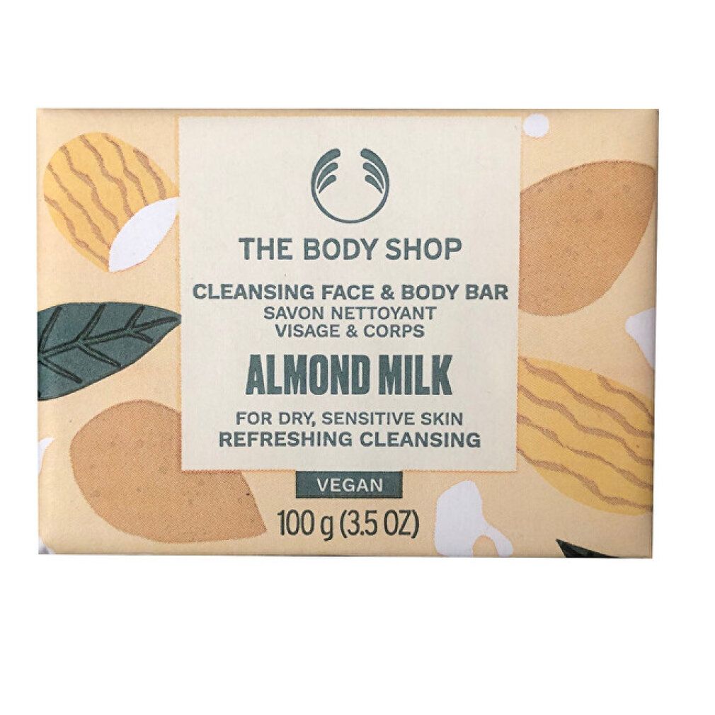 Seifenstück in Papierverpackung. Aufschrift: The Body Shop, Cleansing Face & Body Bar, Almond Milk, Vegan. 100 g.