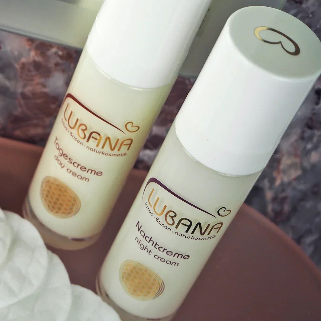 Zwei Creme-Flakons mit weißem Deckel. Aufschrift: Lubana Tagescreme und Nachtcreme. Goldfarbenes Symbol.