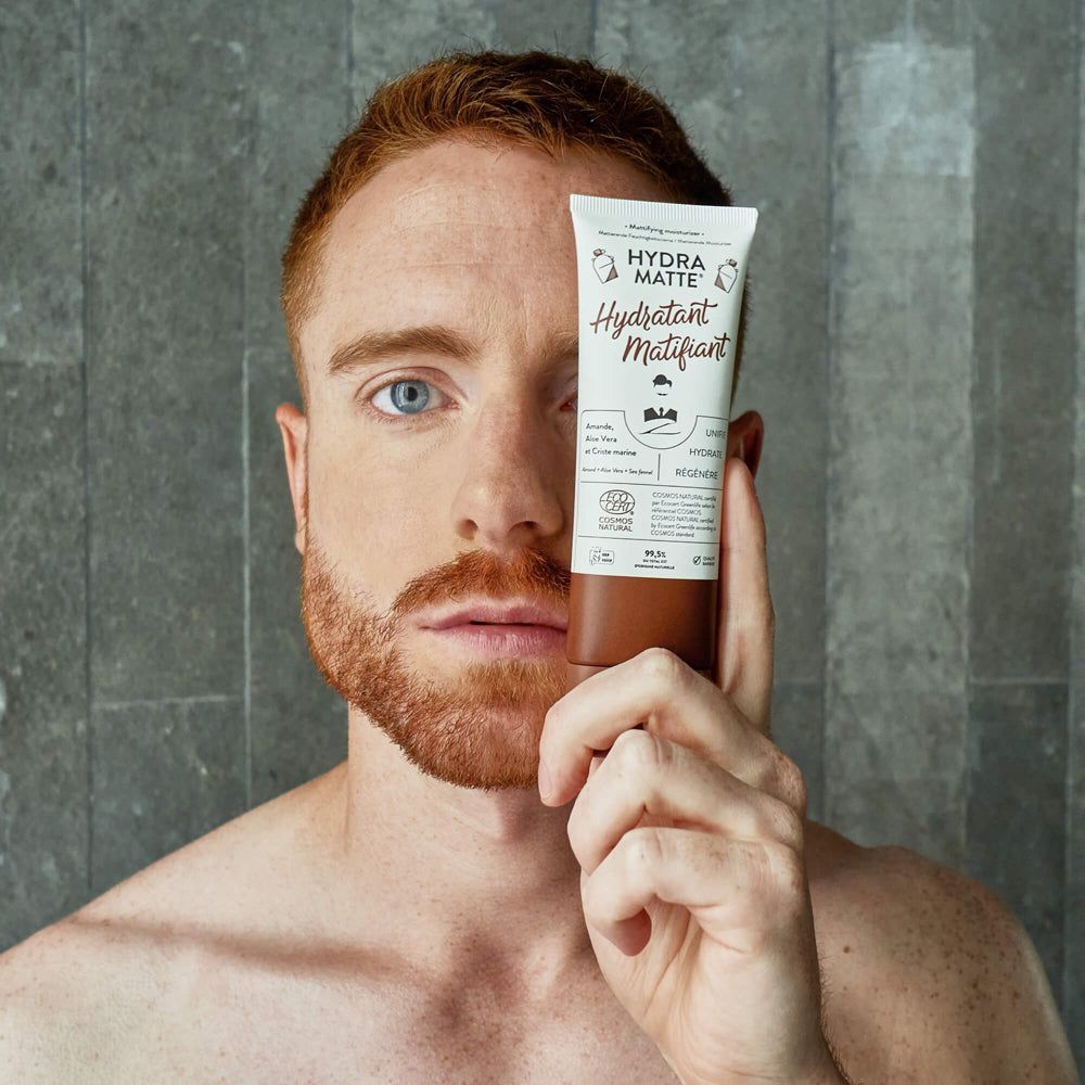 Mann hält Tube vor Gesicht. Auf der Tube steht "Hydra Matte Hydratant Matifiant". Zertifizierungen und Inhaltsstoffe sind ebenfalls sichtbar.