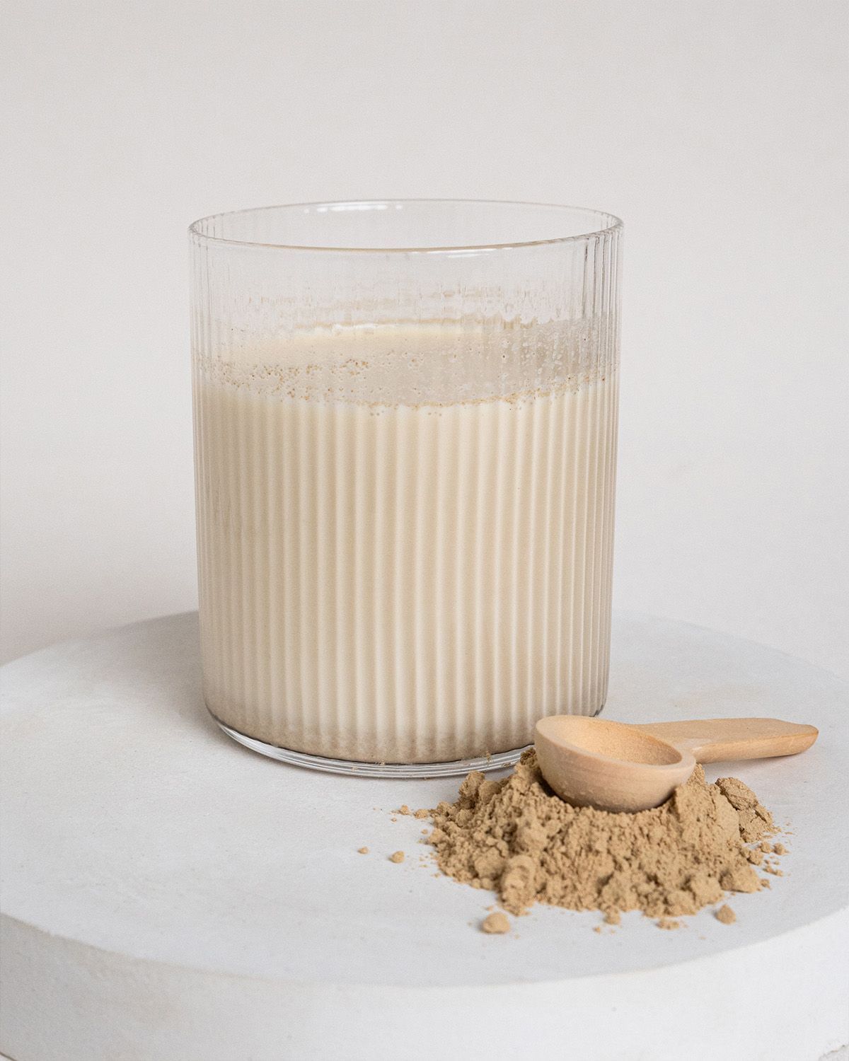 Glas mit Flüssigkeit und braunem Pulver daneben. Kleiner Holzlöffel. Geriffeltes Glas.