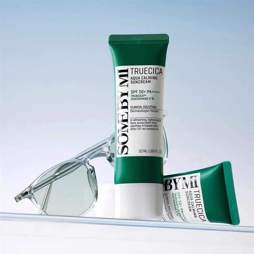 Zwei Tuben Sonnencreme, grüne Kappe, weißer Körper. Text: SOMEBYMI, TRUECICA Aqua Calming Suncream, SPF 50+ PA++++. Brille.