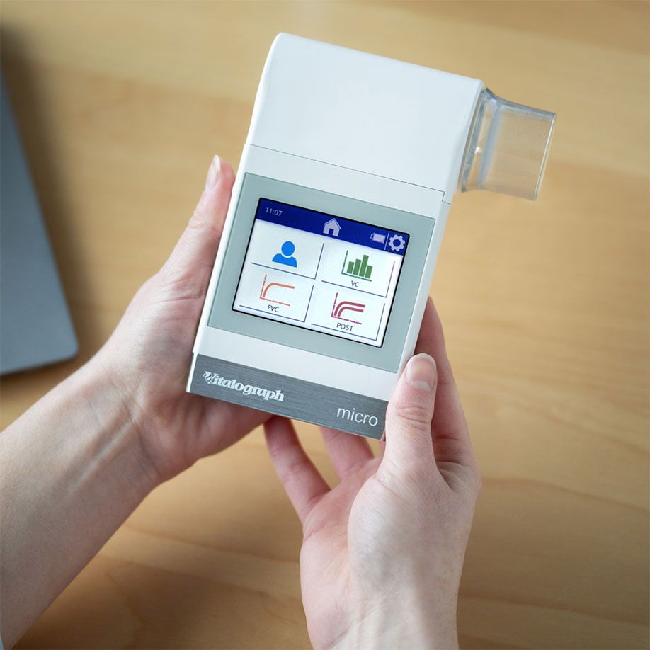 Person hält Vitalograph micro Hand-Spirometer mit Touchscreen-Display, das Lungenfunktionsdiagramme anzeigt.