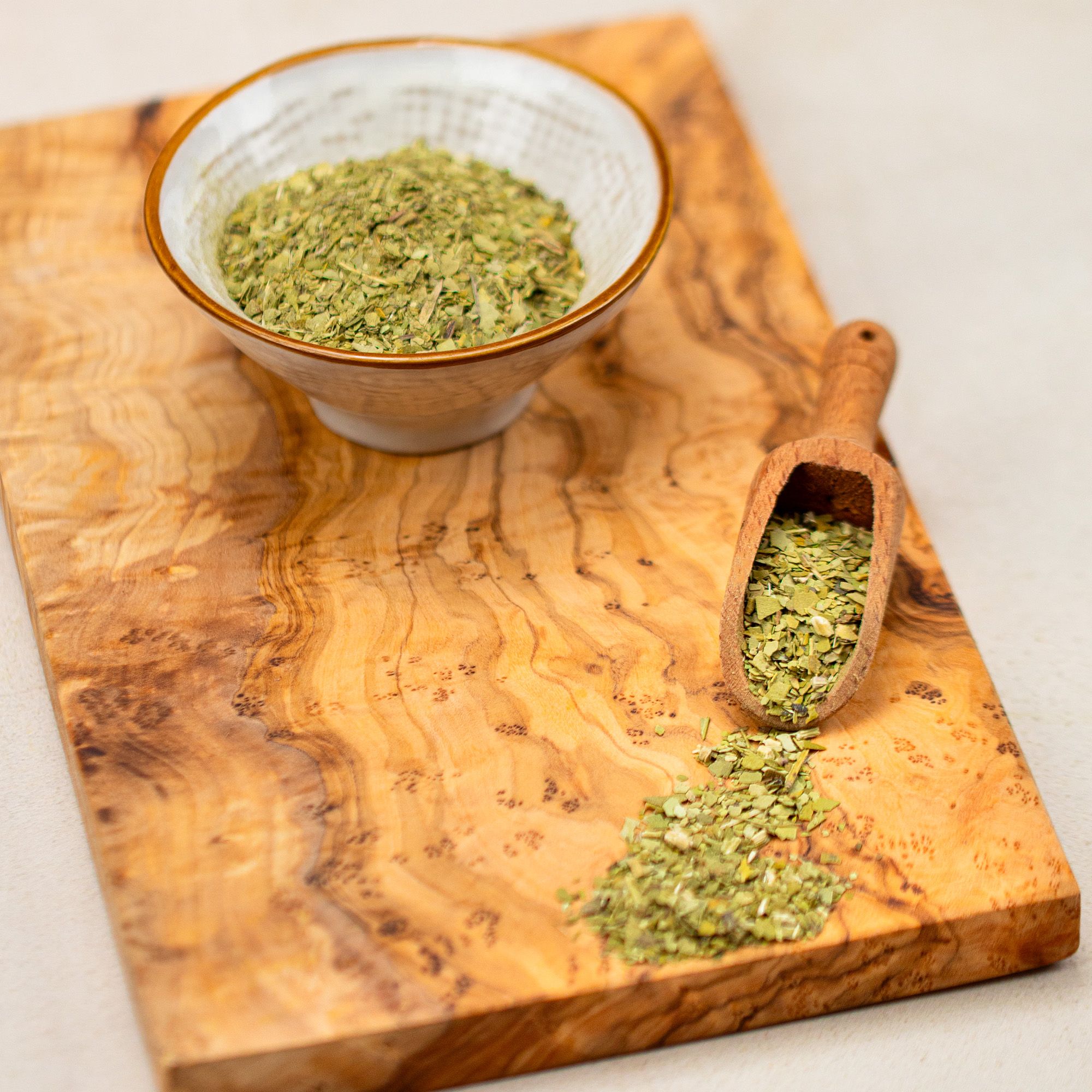 Schale und Holzlöffel mit Mate-Tee auf Holzbrett. Tee verstreut auf dem Brett.