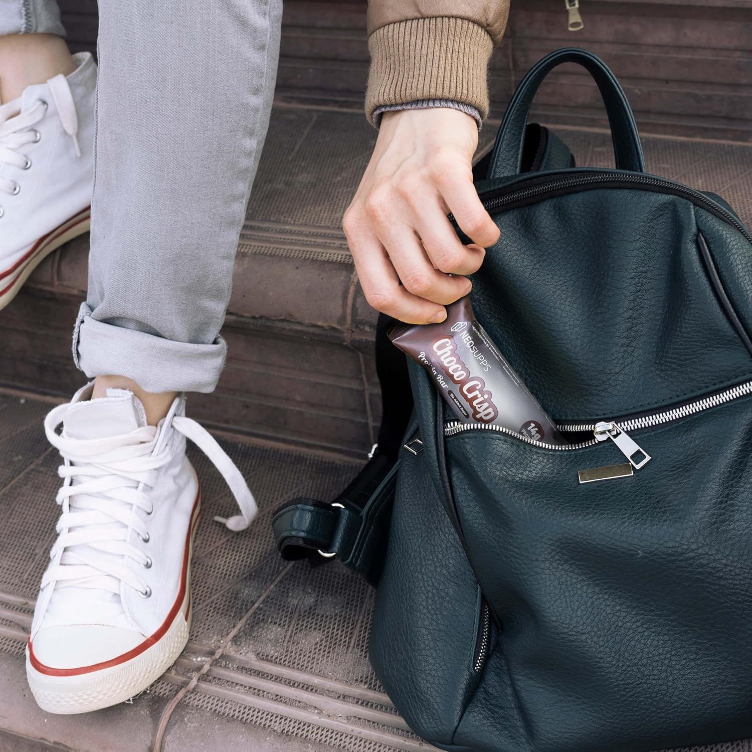 Hand steckt eine Neosupps Choco Crisp Proteinriegel in eine schwarze Tasche.