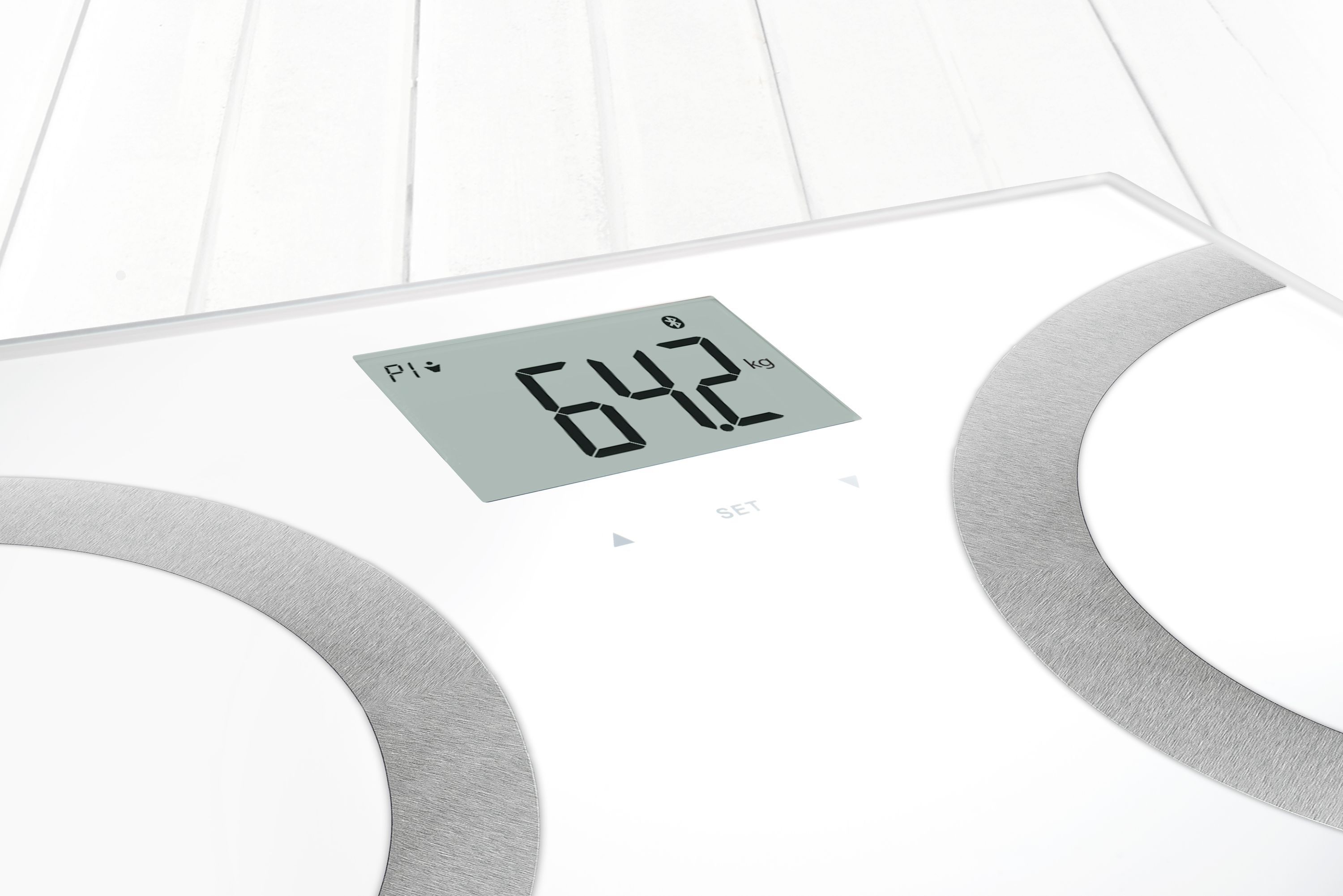 Nahaufnahme einer weißen Körperanalysewaage. Zeigt 64,2 kg auf digitaler Anzeige. Graue, halbkreisförmige Elemente.