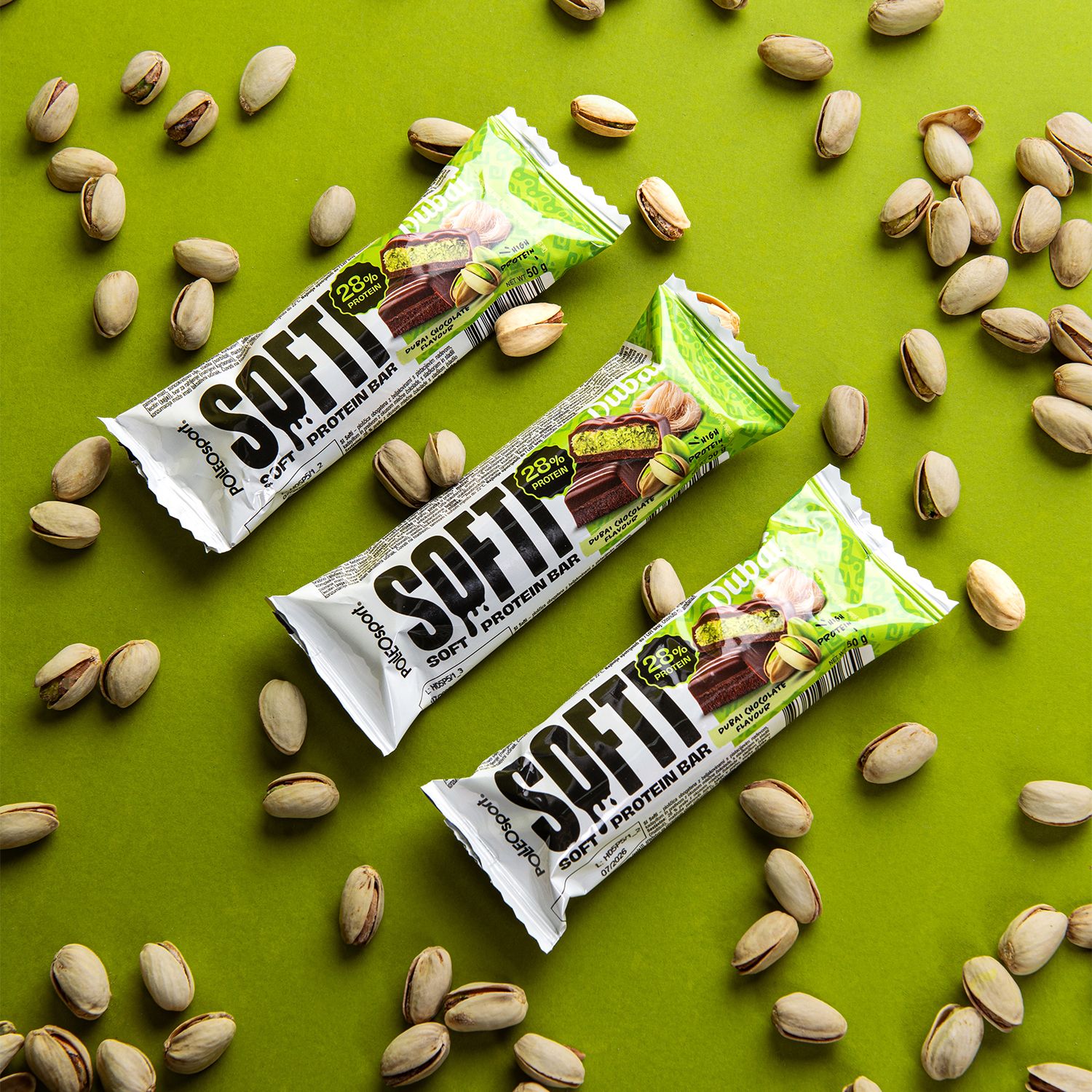 Drei Proteinriegel auf grünem Hintergrund. Aufschrift "SOFTI PROTEIN BAR". 28% Protein. Umgeben von Pistazien.