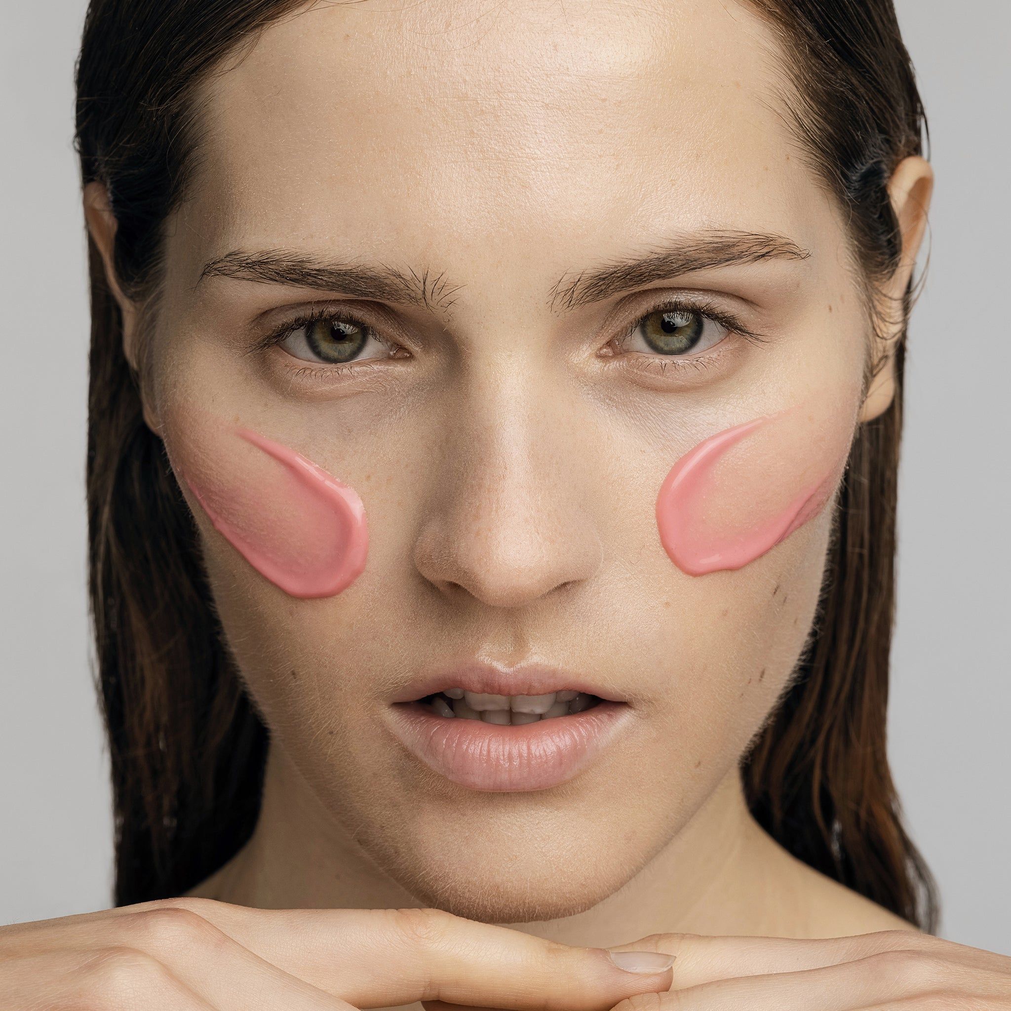 Gesicht mit rosa Serum auf beiden Wangen. Haut mit Sommersprossen. Blick in die Kamera.