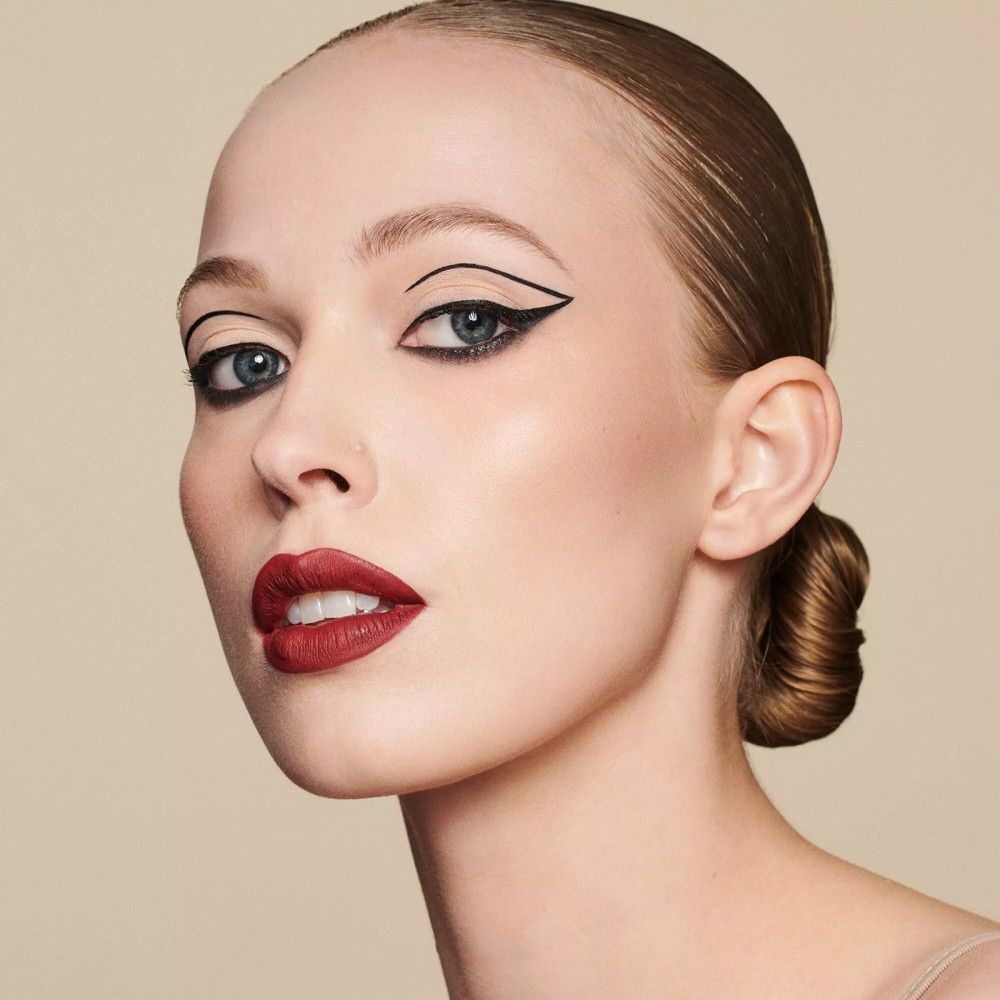 Porträt einer Frau mit aufgetragenem Eyeliner. Roter Lippenstift und hochgesteckte Haare.