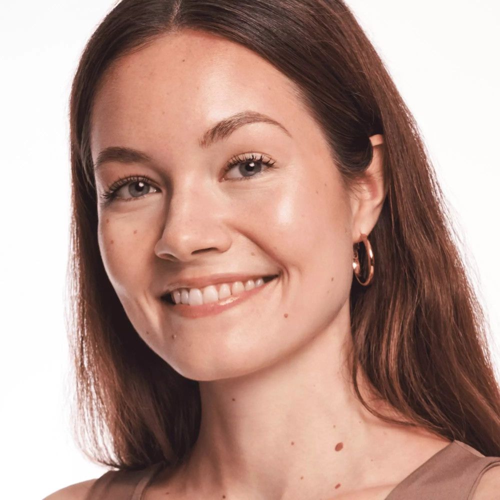 Porträt einer lächelnden Frau. Sie trägt Ohrringe und hat einen natürlichen, strahlenden Teint.