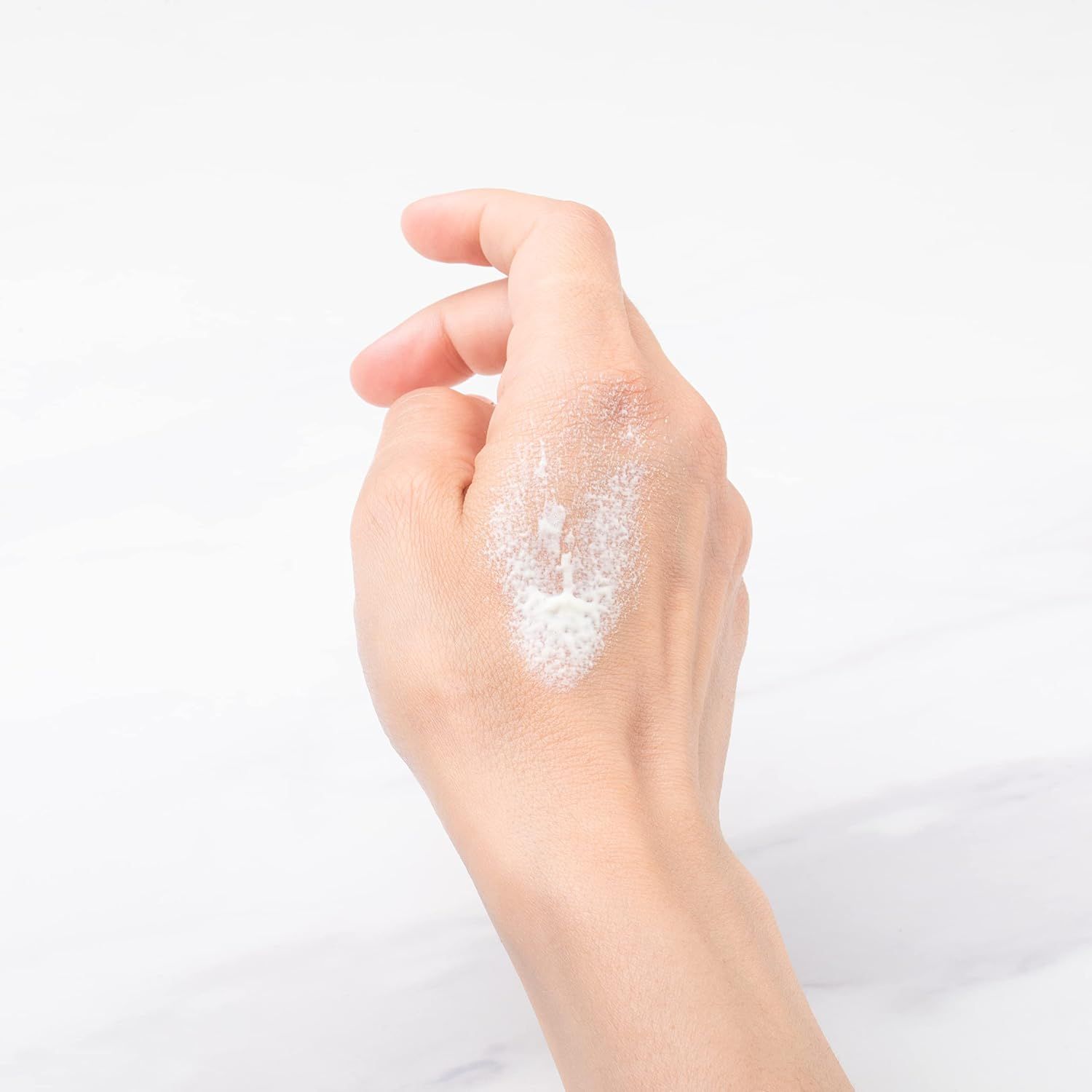 Hand mit weißem Schaum auf Marmoruntergrund.