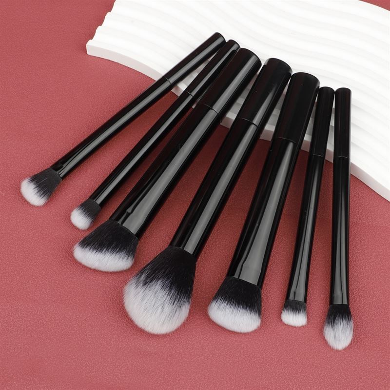 Sieben schwarze Make-up-Pinsel mit weißen Borsten, auf weißem Hintergrund. Unterschiedliche Formen.