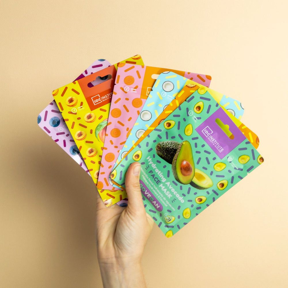 Hand hält mehrere bunte Gesichtsmasken. Verschiedene Designs mit Avocado, Kokosnuss und anderen Früchten.