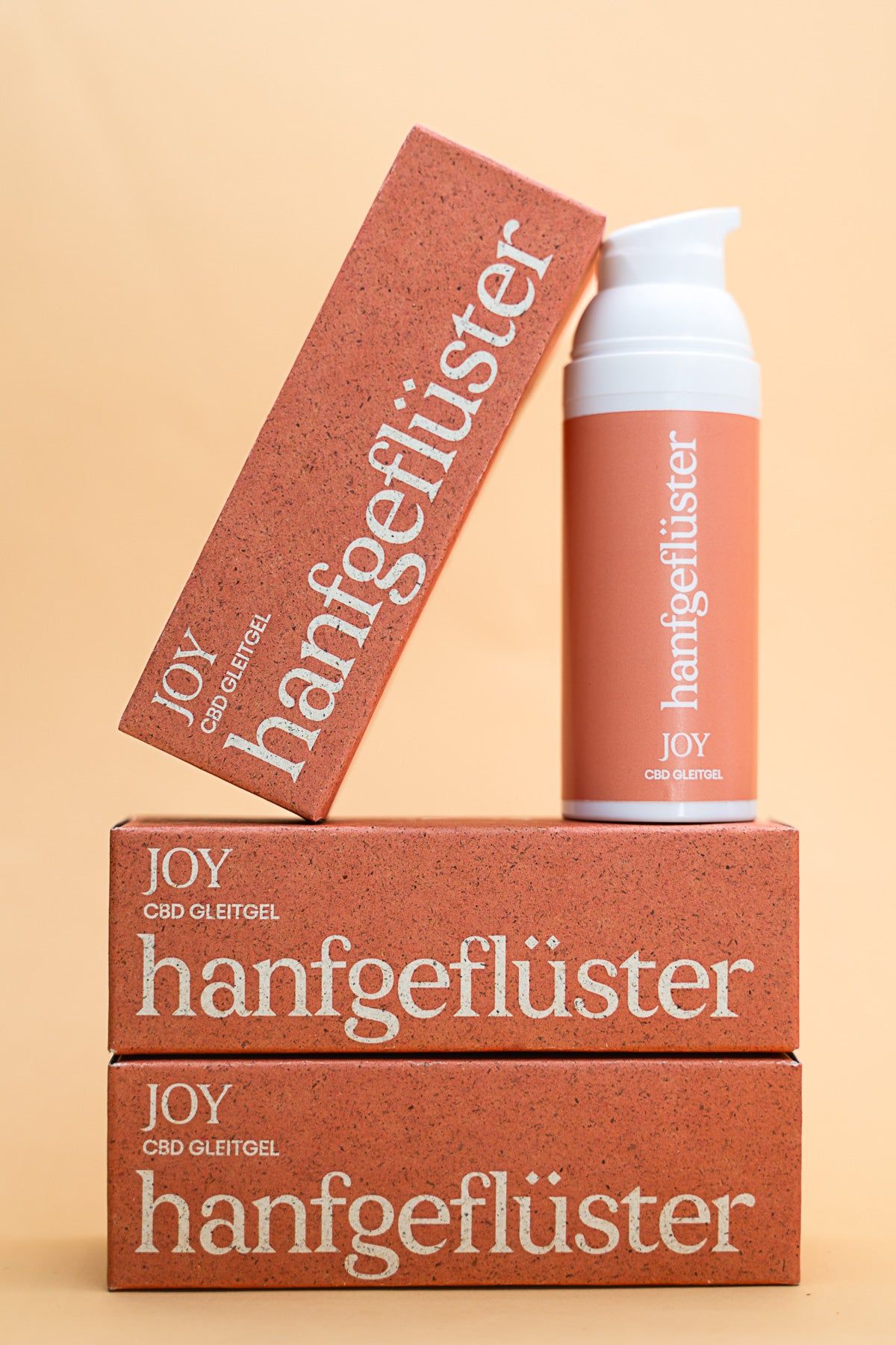 Zwei Verpackungen und eine Flasche. Aufschrift: hanfgeflüster JOY CBD Gleitgel. Orangefarben mit weißer Schrift.
