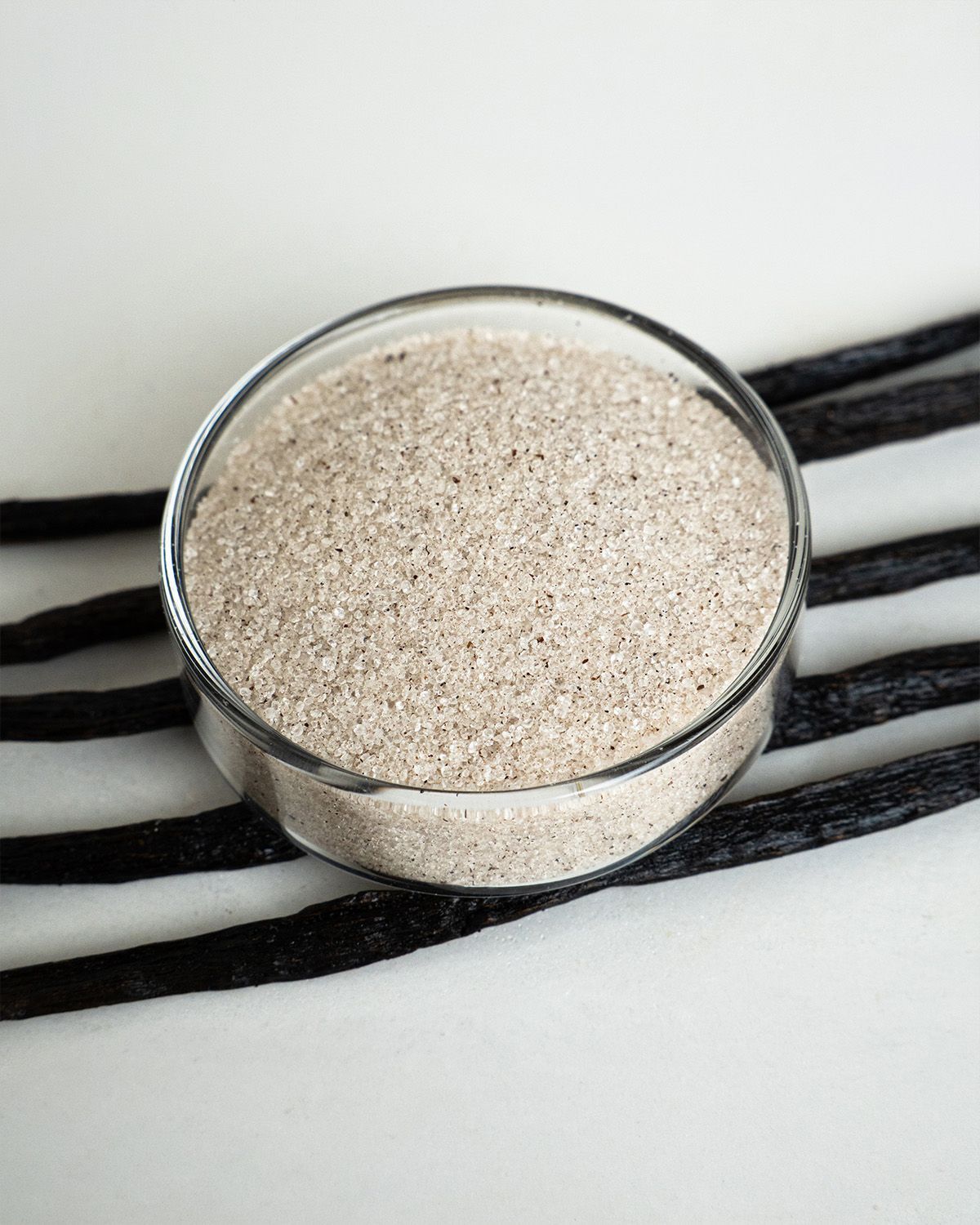 Erythritol Vanille in einem Glasbehälter, daneben liegen drei Vanilleschoten.