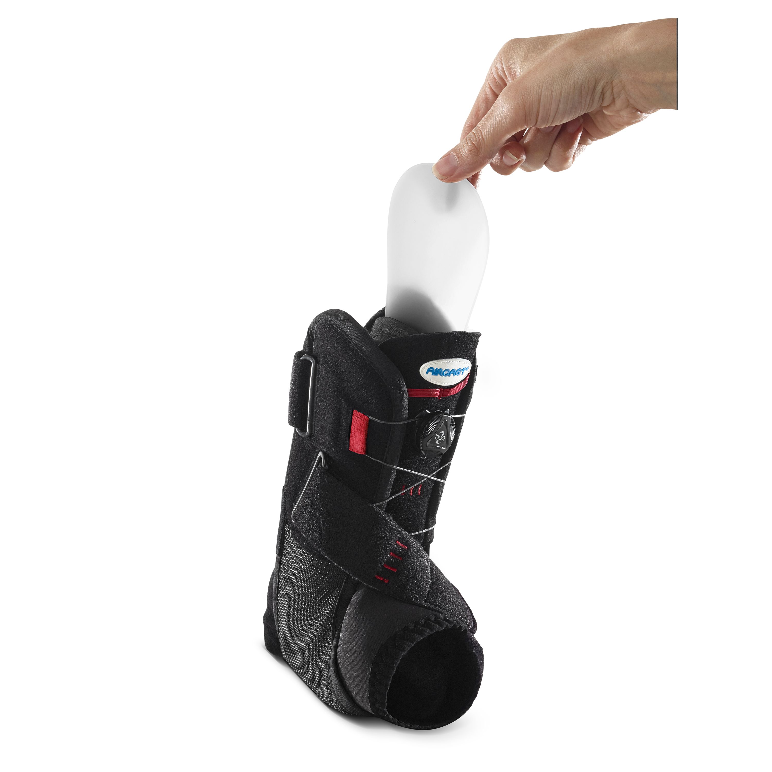 Schwarze AIRCAST® AIRPRO Sprunggelenkorthese. Eine Hand hält eine weiße Einlegesohle. Rote Akzente und Schnürsystem.