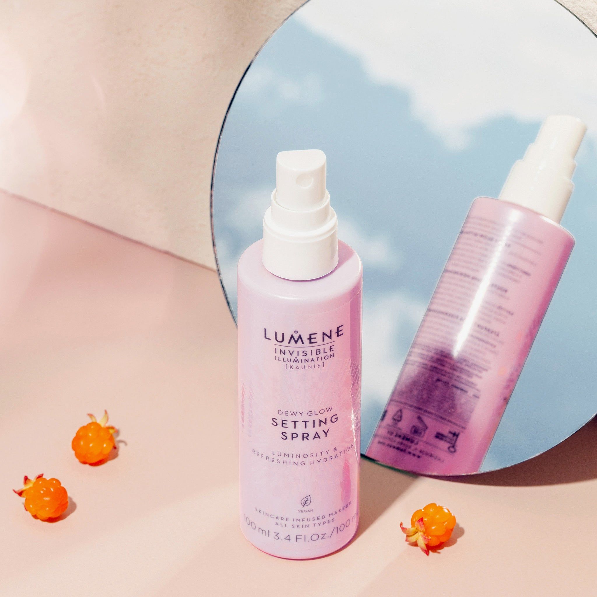 Zwei rosa Flaschen mit weißem Sprühkopf. Aufschrift: Lumene INVISIBLE ILLUMINATION Dewy Glow Setting Spray. Spiegelung im Spiegel. Beeren.