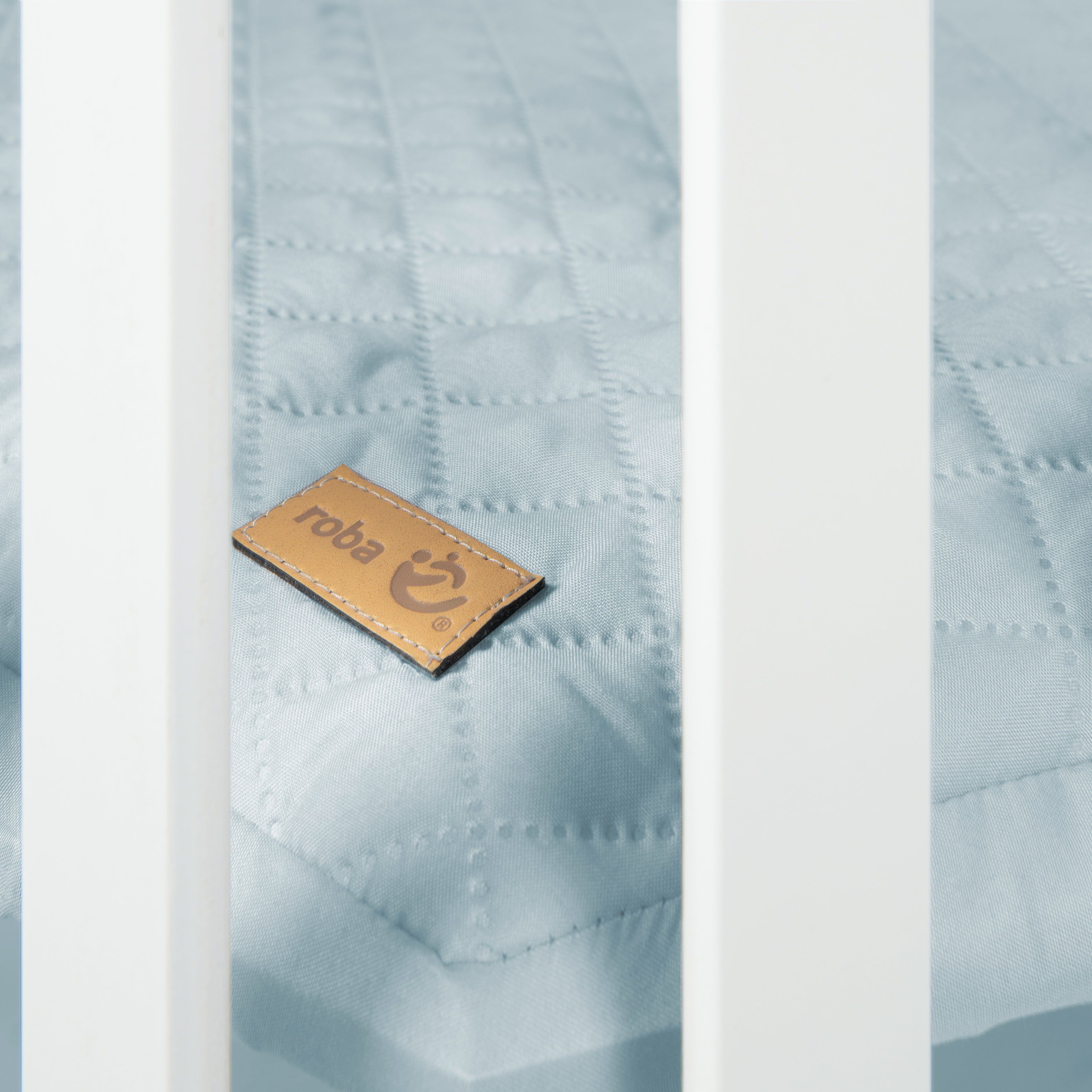 Nahaufnahme des blauen Stoffes im Laufgitter. Lederetikett mit 'roba' Logo. Gestepptes Muster.