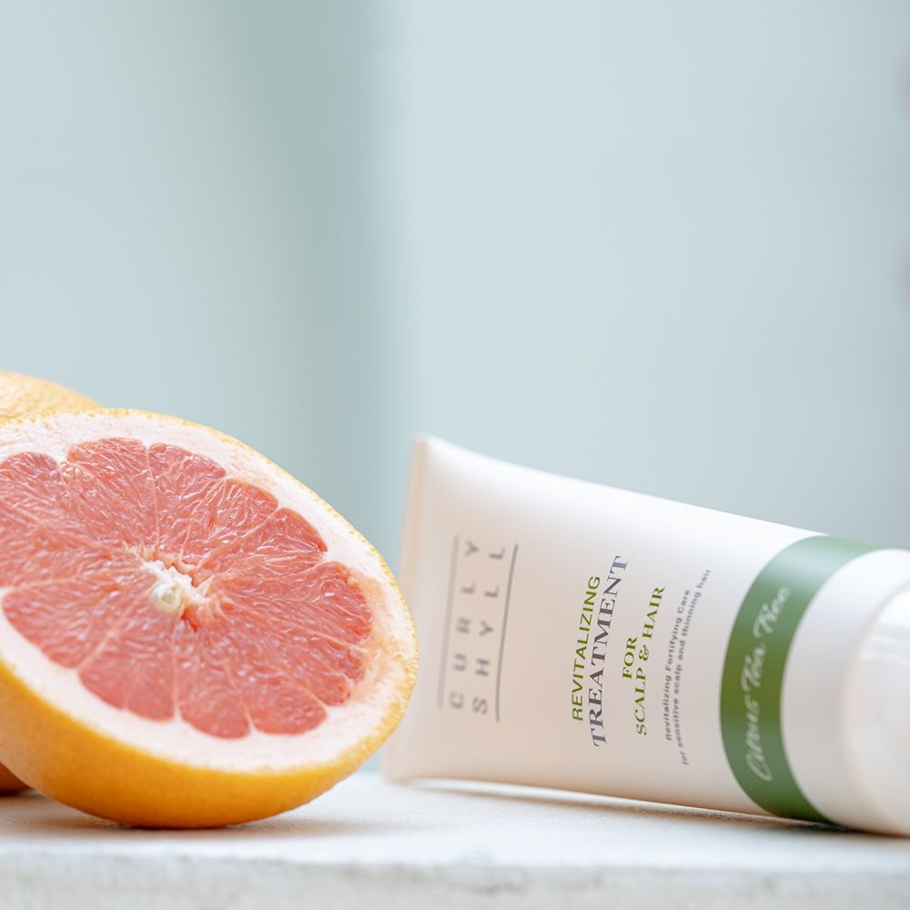 Beige Tube neben Grapefruit-Hälfte. Produktname und Text sichtbar. Grüner Streifen mit "Citrus Tea Tree".