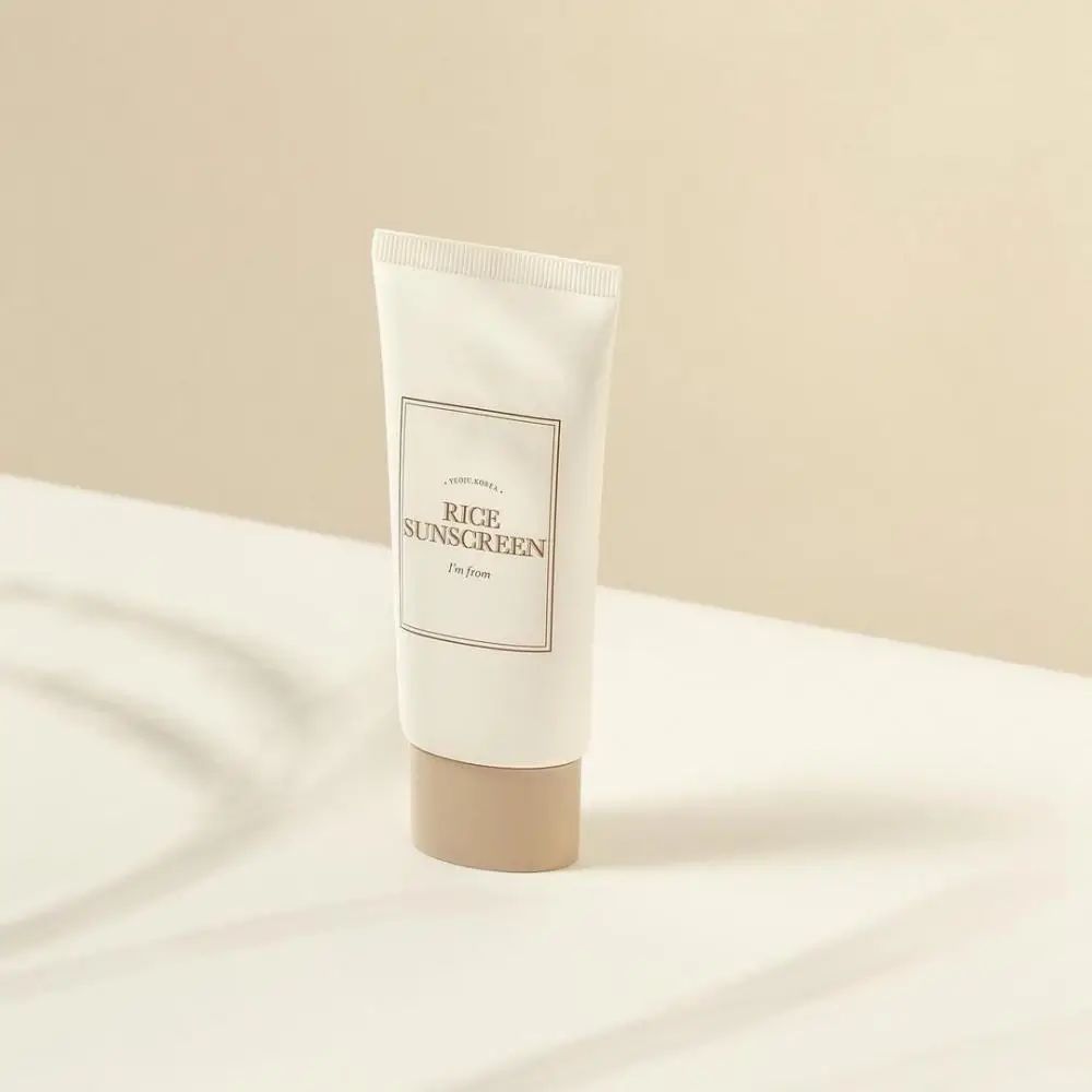 Creme-Tube mit Aufschrift „Rice Sunscreen“ und „I'm from“. Beige Kappe auf weißem Hintergrund.
