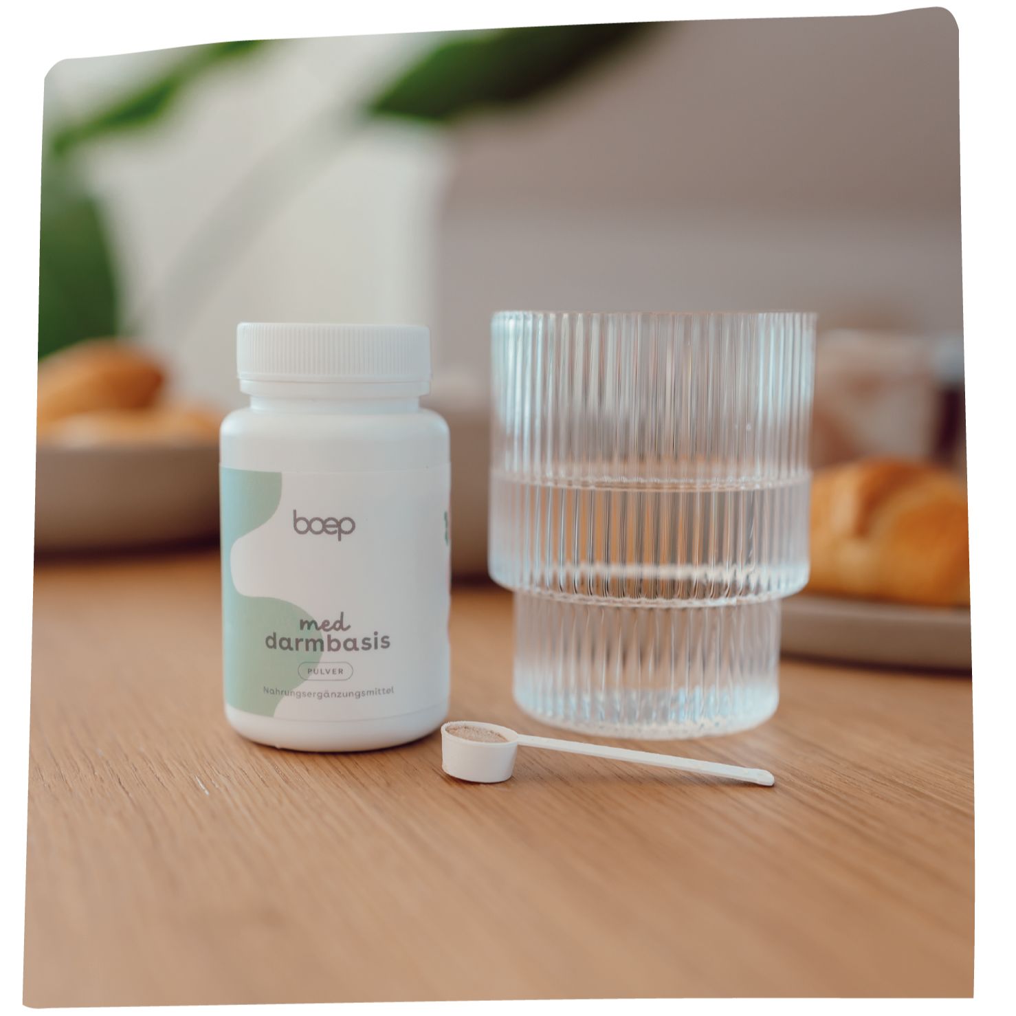 Weißes boep Med Darmbasis Pulver-Behältnis, Glas mit Wasser, kleiner Löffel. Aufschrift und Logo sichtbar.