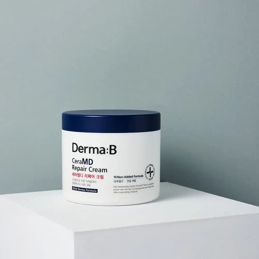 Weißer Tiegel mit blauem Deckel. Aufschrift: Derma:B CeraMD Repair Cream. Auf weißer Oberfläche vor blauem Hintergrund.