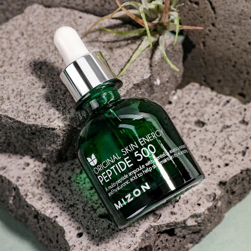 Grüne Glasflasche mit Pipette auf Stein. Aufschrift: ORIGINAL SKIN ENERGY PEPTIDE 500, MIZON.