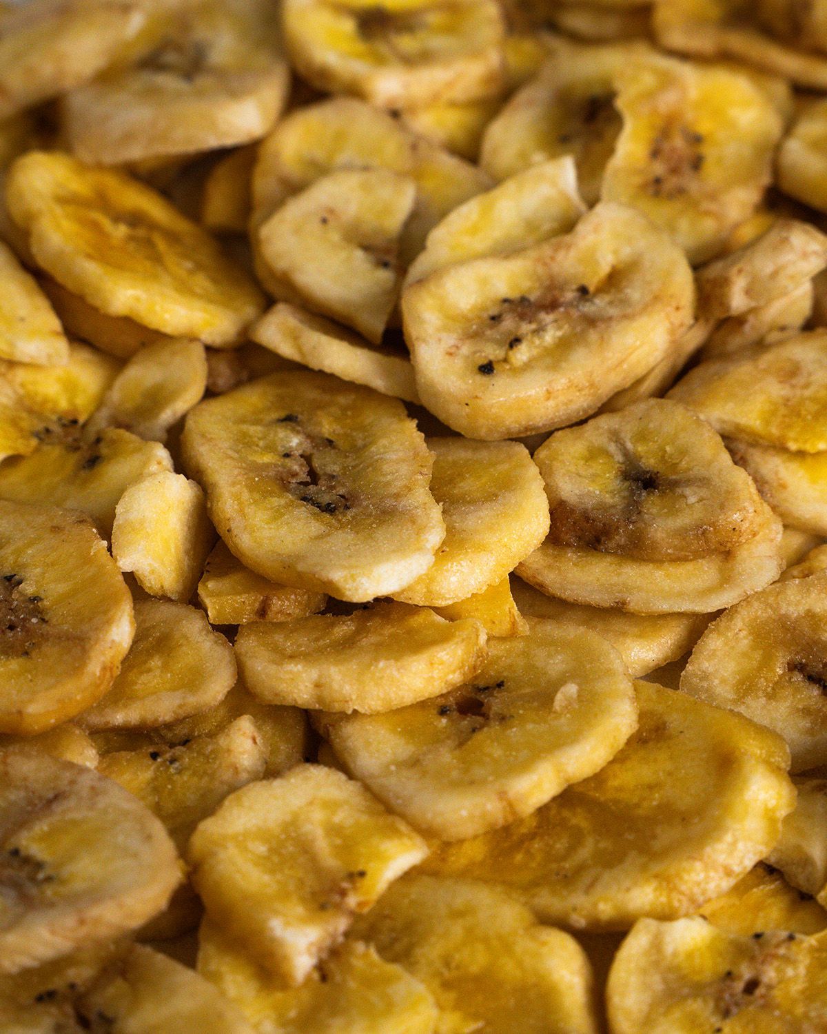 Nahaufnahme von Bio Bananenchips. Gelbliche, runde Chips mit dunklen Punkten. Chips liegen lose.