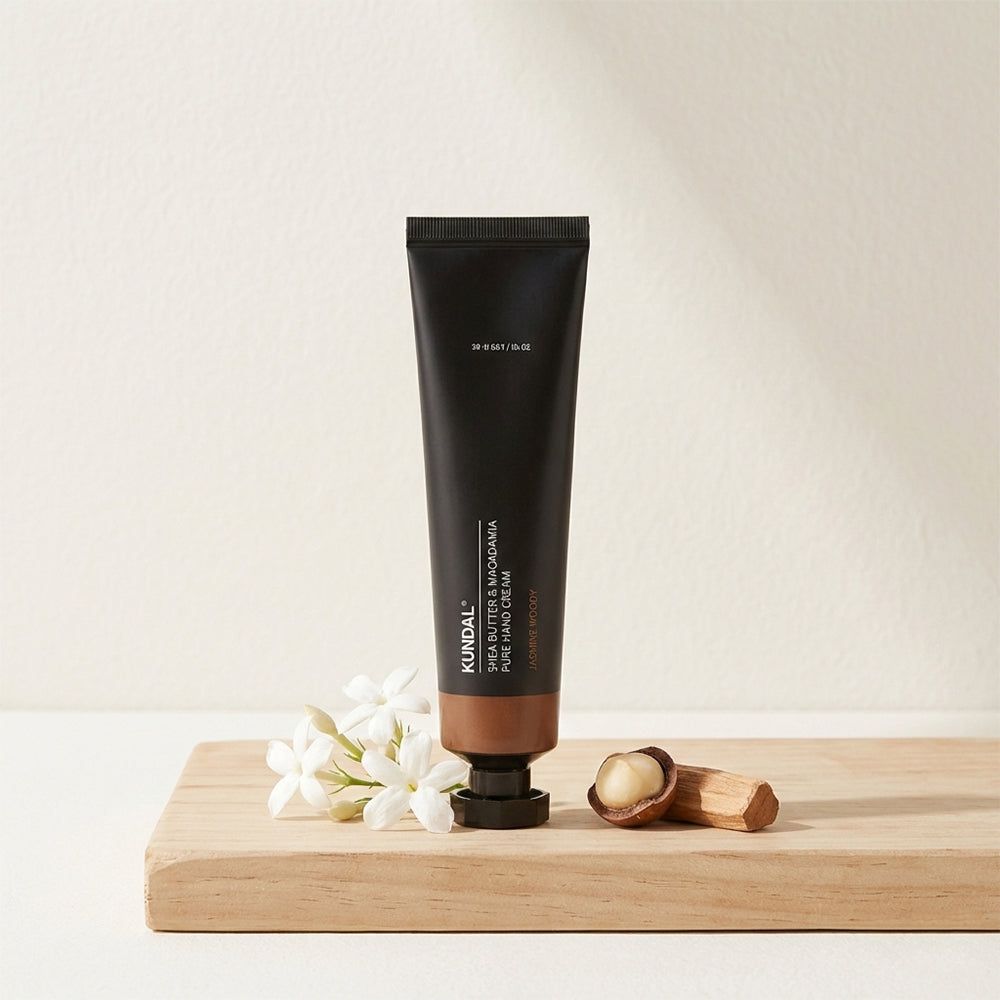 KUNDAL Handcreme Tube mit Macadamianüssen und Blüten auf Holzbrett.