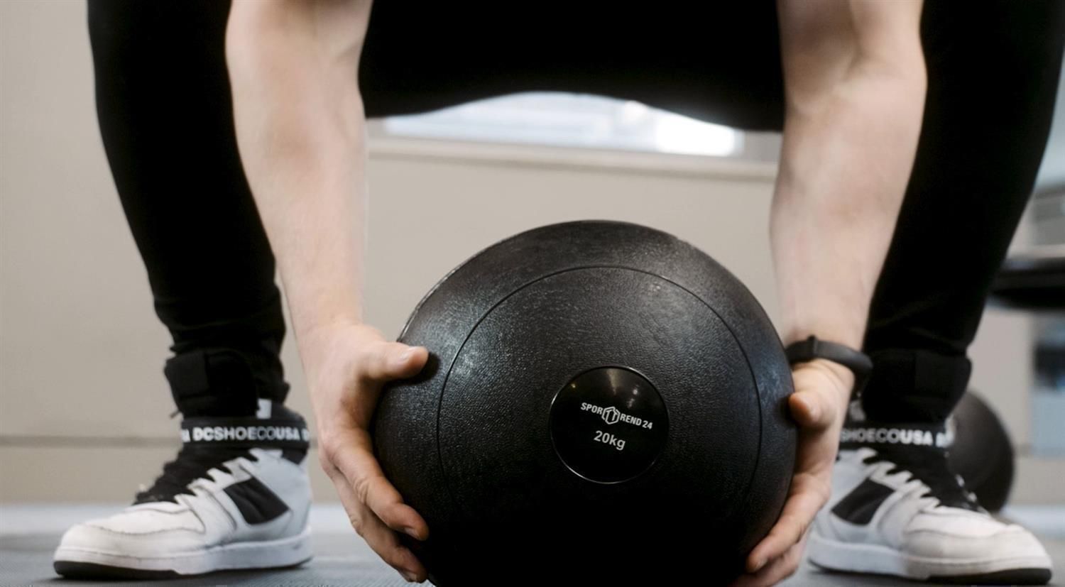 Nahaufnahme einer Person, die einen schwarzen Slamball hält. Auf dem Ball steht Sporttrend24 und 20kg.