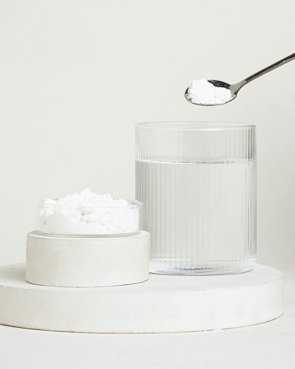 D-Mannose powder in a small container, on a spoon, and in a glass of water.