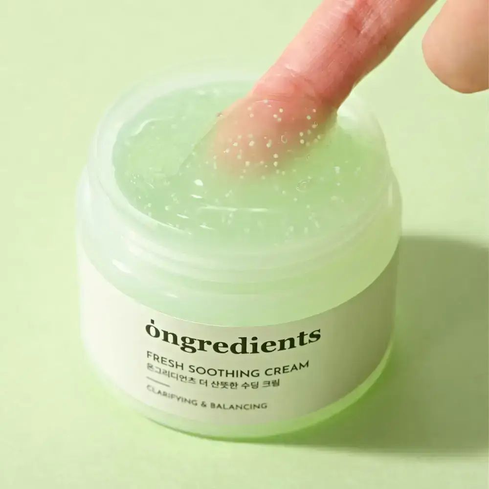 Offenes Creme-Glas mit grüner Creme. Ein Finger berührt die Creme. Aufschrift: ONGREDIENTS, FRESH SOOTHING CREAM, koreanischer Text, CLARIFYING & BALANCING.