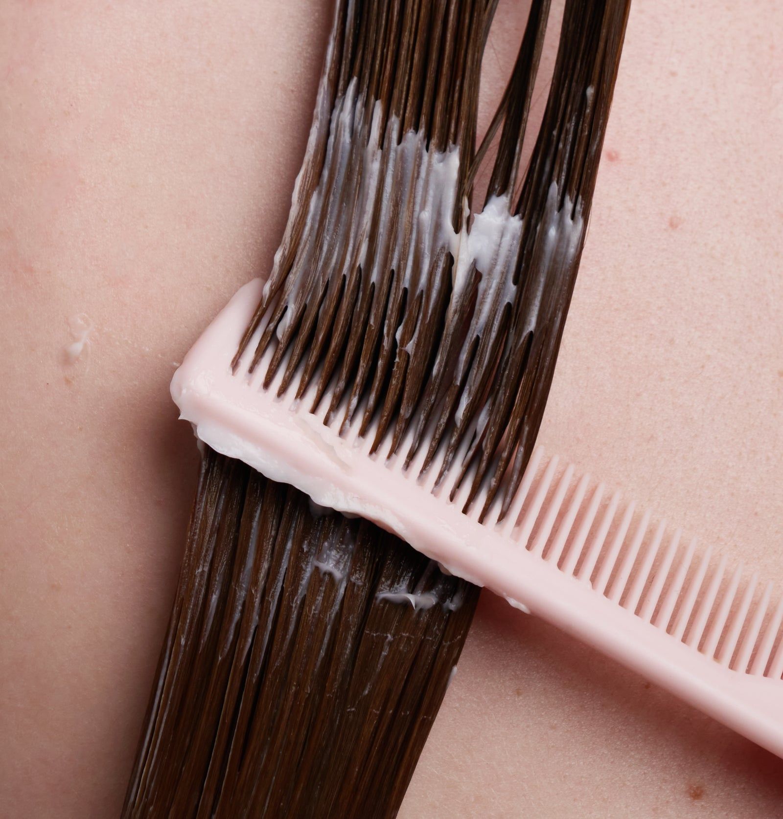 Haarsträhne mit aufgetragener Creme und Kamm. Der Kamm ist rosa. Die Creme ist weiß.