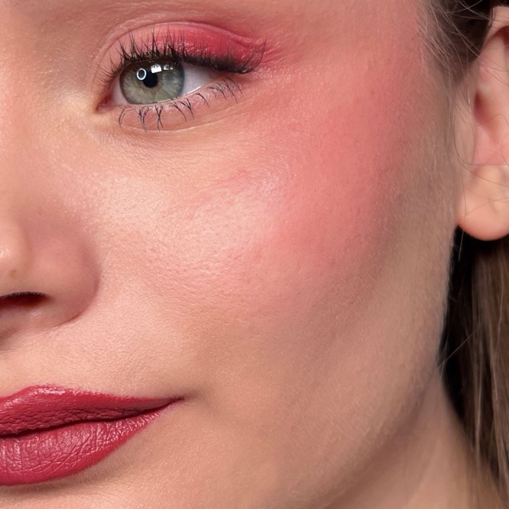 Nahaufnahme eines Gesichts mit Make-up. Roter Lidschatten, Rouge und Lippenstift. Grünes Auge.