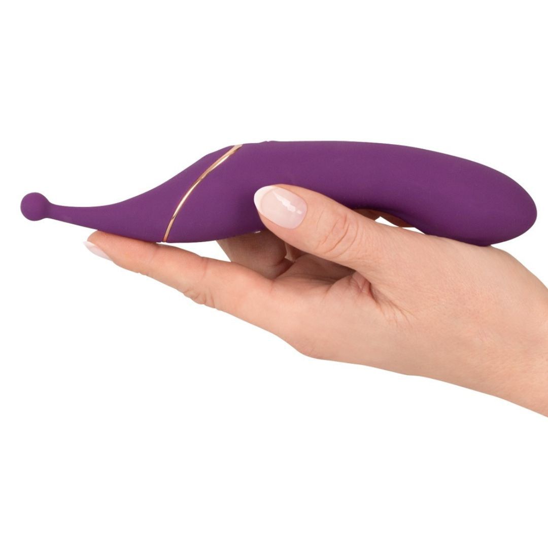 Lila Vibrator in einer Hand gehalten. Geschwungene Form, goldfarbene Akzente. Tropfenförmiger Kopf.