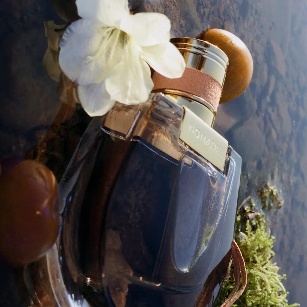 Parfümflasche im Wasser. Flasche mit goldener Kappe und Anhänger. Dekoration mit Blumen und Früchten.
