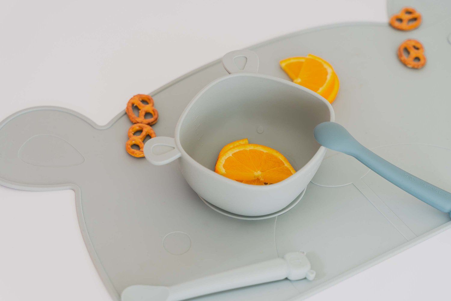 Platzset in Eisberg-Farbe mit Bärenform. Darauf eine Schüssel mit Orangenscheiben, Löffel und Brezeln.