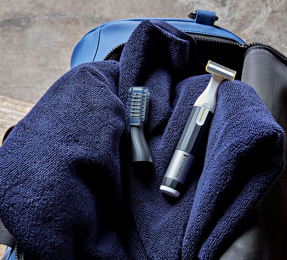 Trimmer und Aufsatz auf blauem Handtuch in einer blauen Tasche. Der Trimmer hat einen silbernen Bereich mit dem Markennamen Remington.