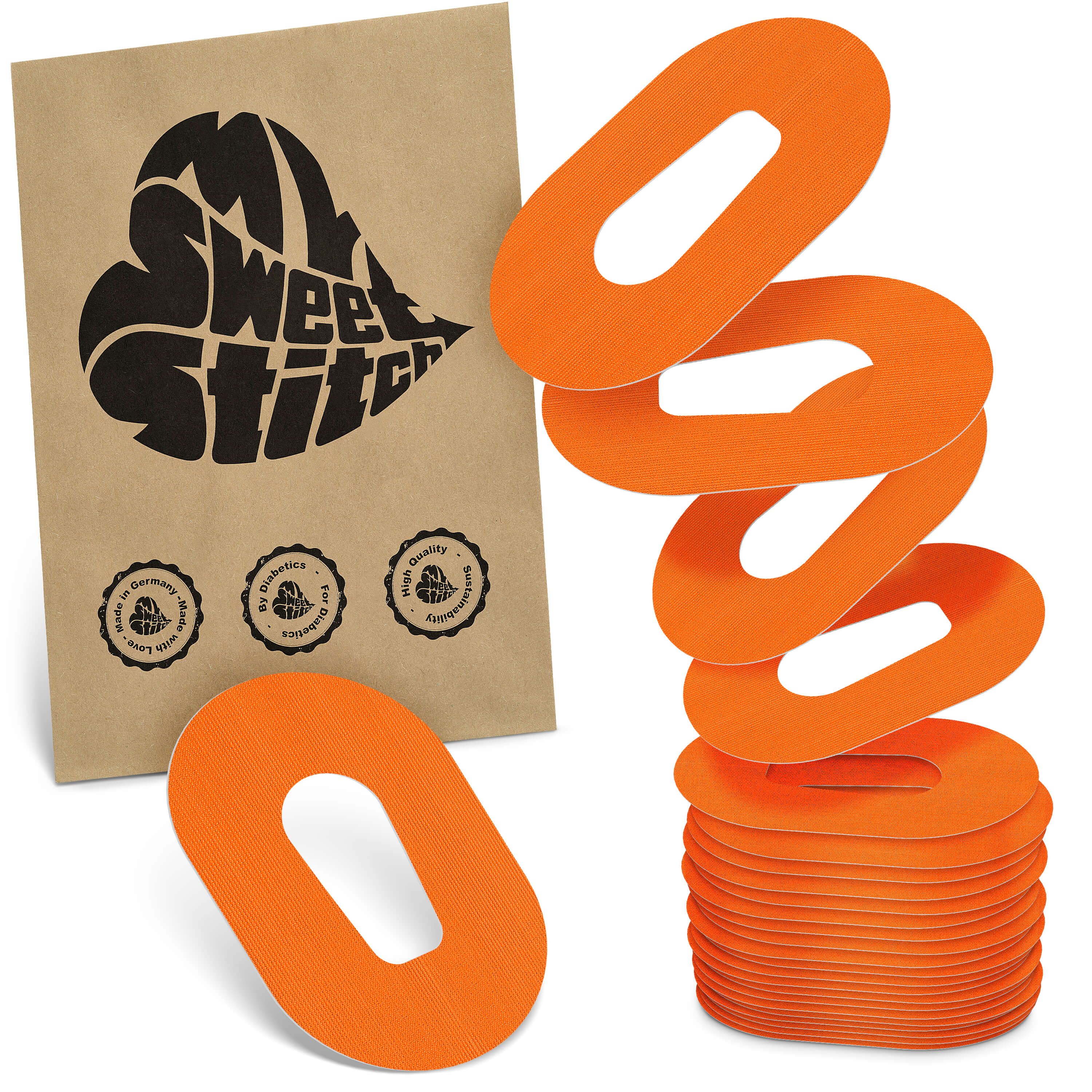 Orange, ovale Pflaster mit Loch in der Mitte, gestapelt und einzeln liegend, neben einer braunen Papiertüte mit schwarzem Herz-Logo.