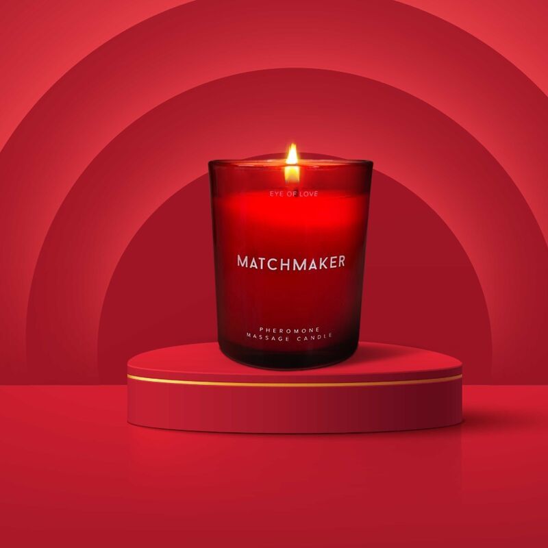 Rote Kerze im Glas auf Podest. Aufschrift: MATCHMAKER, EYE OF LOVE, Pheromone Massage Candle. Brennende Flamme.