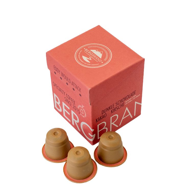 Drei Kaffeekapseln neben einer roten Verpackung. Aufdruck: BERGBRAND, Eddy would Attack, Kapselkaffee.