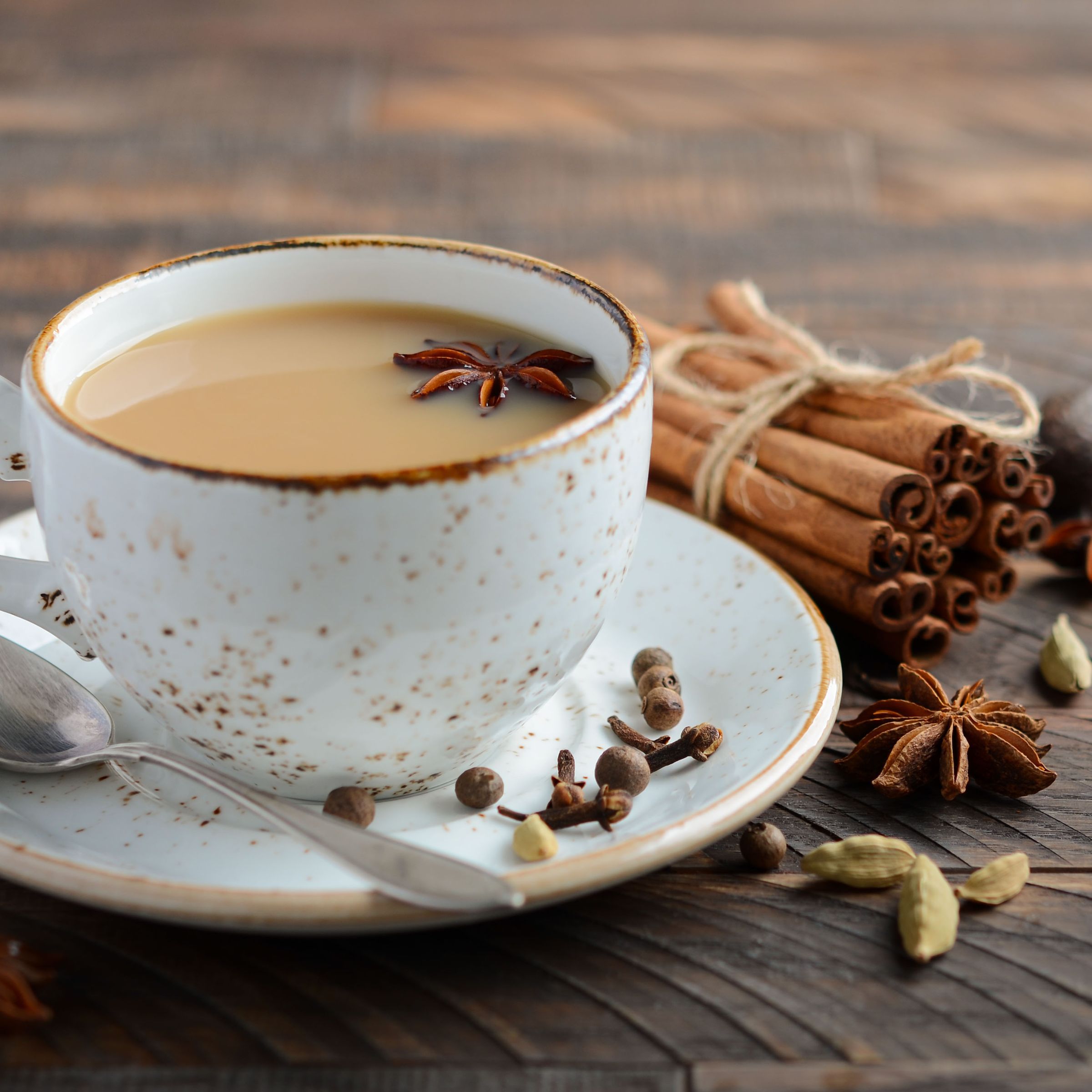Tasse Tee mit Sternanis und Zimtstangen. Auf einem Unterteller mit Löffel. Auf einem Holztisch.