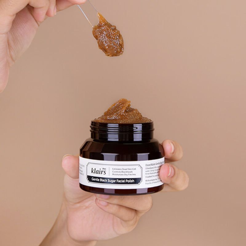 Glas mit brauner Creme, Löffel mit Creme darüber. Aufschrift: dear, klairs Gentle Black Sugar Facial Polish.
