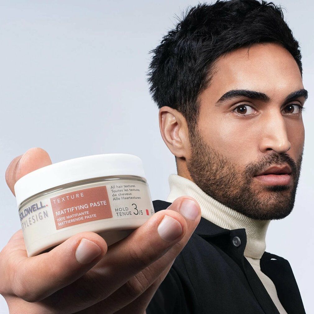 Mann hält Goldwell Stylesign Texture Mattierende Paste. Produktname und Marke sichtbar. Weißer Deckel, beige Dose.