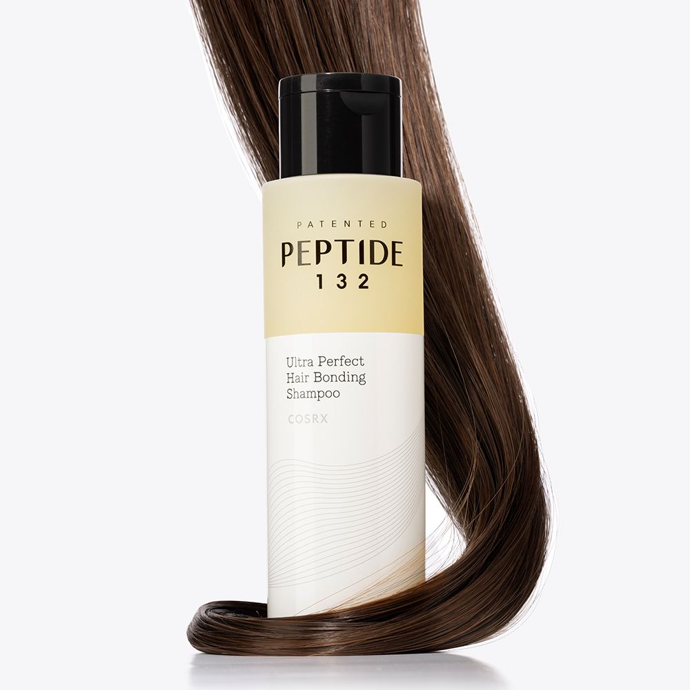 Flasche COSRX Peptide 132 Ultra Perfect Hair Bonding Shampoo, umgeben von dunklem Haar.