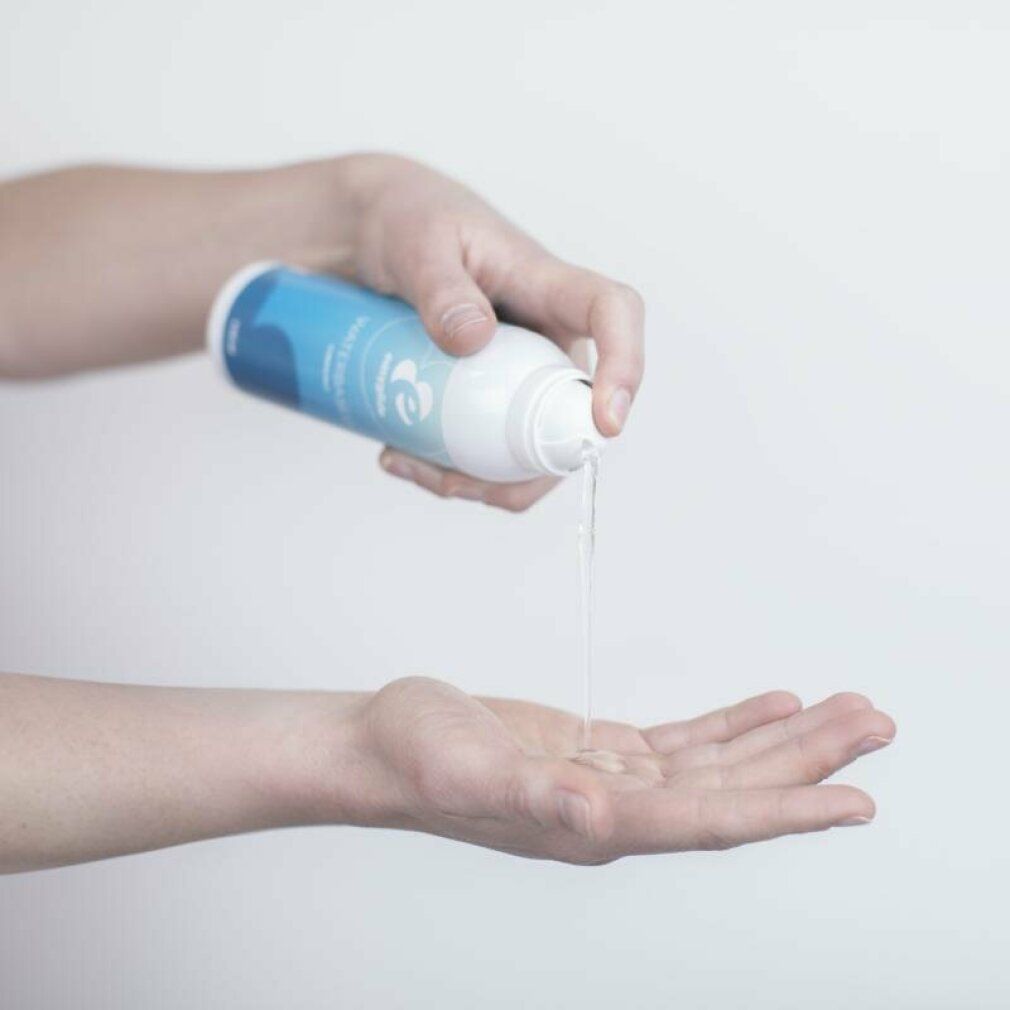 Person hält eine Flasche und gibt eine klare Flüssigkeit in die Handfläche. Die Flasche ist blau-weiß und trägt die Aufschrift "WATERBASED".