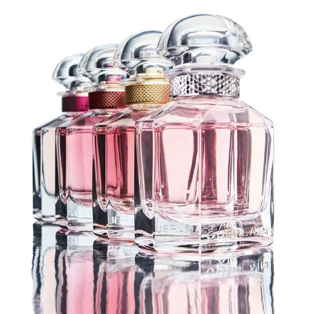 Reihe von Parfümflakons mit rosa Flüssigkeit. Flakons mit Kristallbesatz und Deckel. Reflektierender Hintergrund.