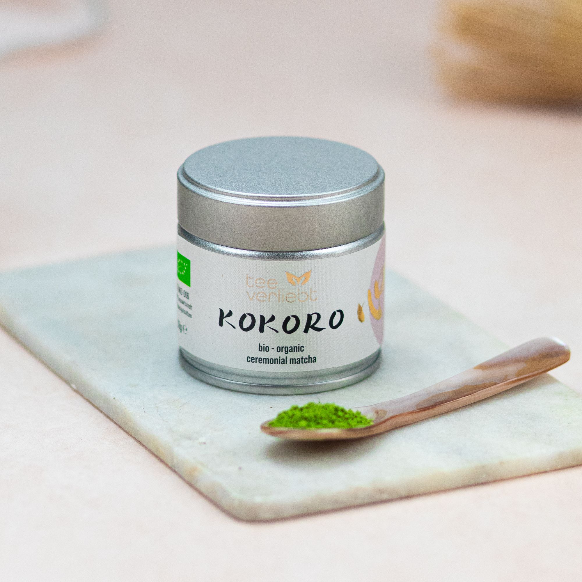 Dose "teeverliebt Kokoro" auf Steinplatte. Löffel mit Matcha-Pulver. Bio-Siegel. Aufschrift "bio - organic ceremonial matcha".