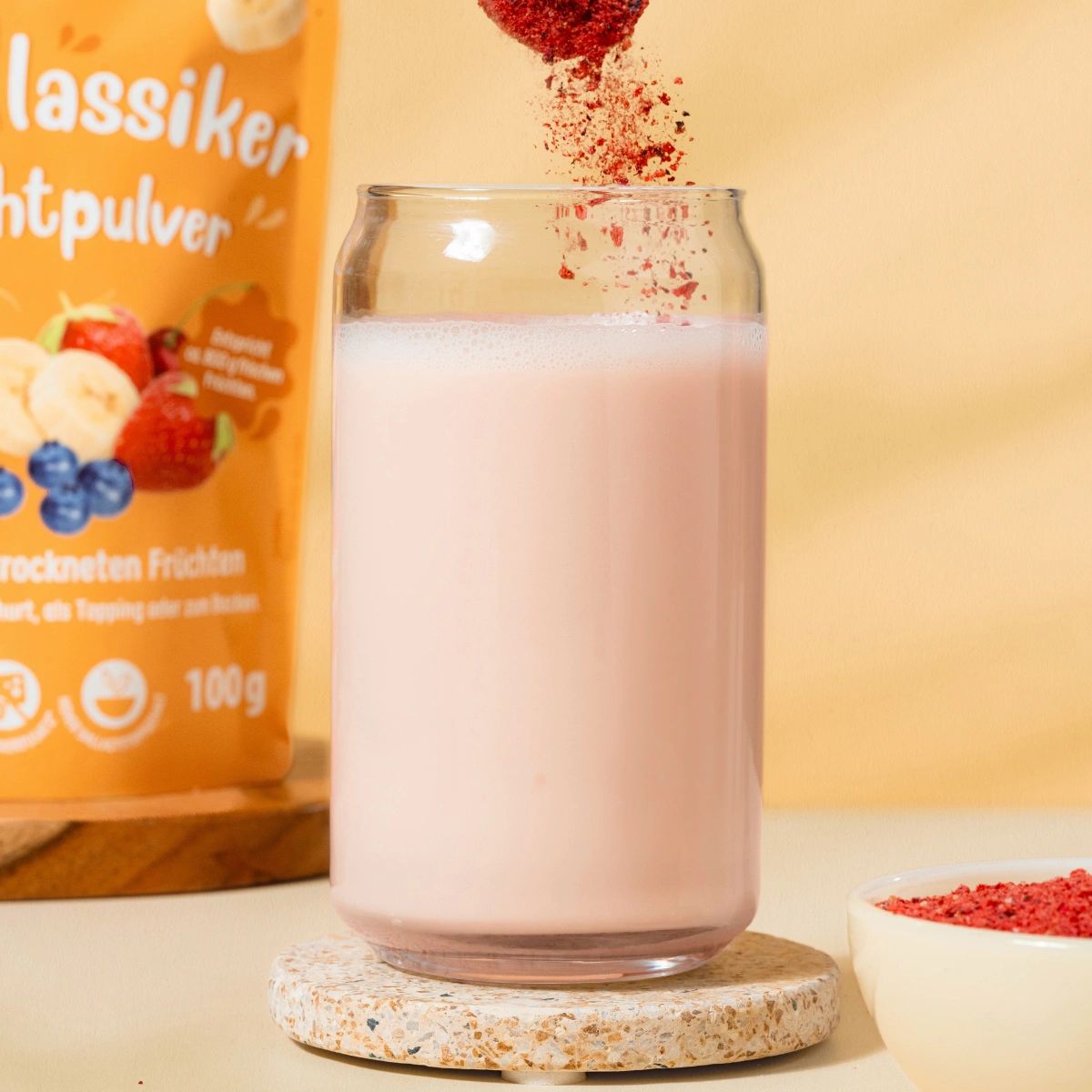 Glas mit rosa Flüssigkeit, Fruchtpulver wird hineingegossen. Daneben Verpackung NutriPur Fruchtpulver und Schale mit rotem Pulver.